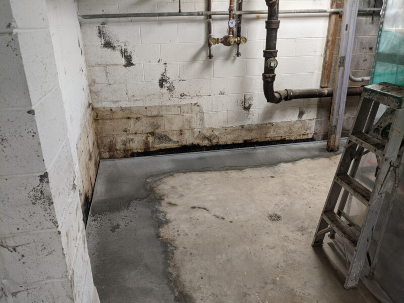 This photo was taken shortly after the initial work was completed for waterproofing. Visible are the non-painted areas of concrete where prior concrete structure/barrier was installed in a (failed) attempt to divert water intrusion. Also visible is the poor state of the walls prior to crack repair. Northwest Basement Corner in January 2021