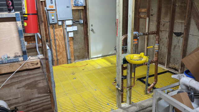 A view of the new floor (and piping, with eye wash) from the concrete floor side of the pump house on January 11th, 2021. New Floor (Alternate View)