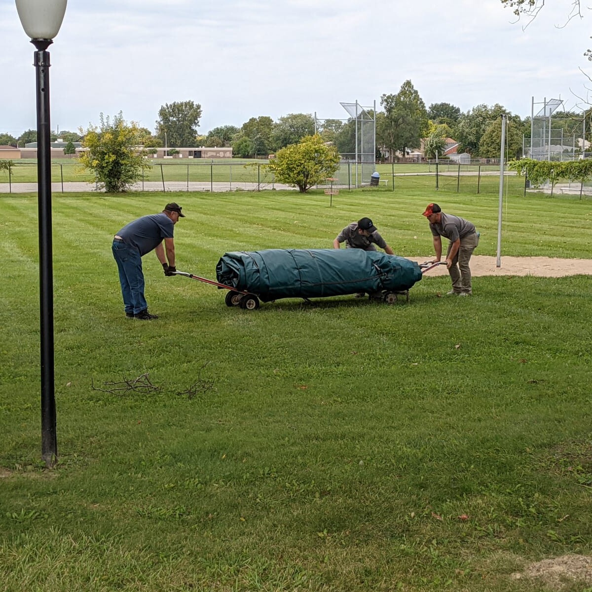 A crew of three from Aquatic Source uses two hand trucks to wheel the cover out from the shed onto the pool deck. Bringing out the Cover